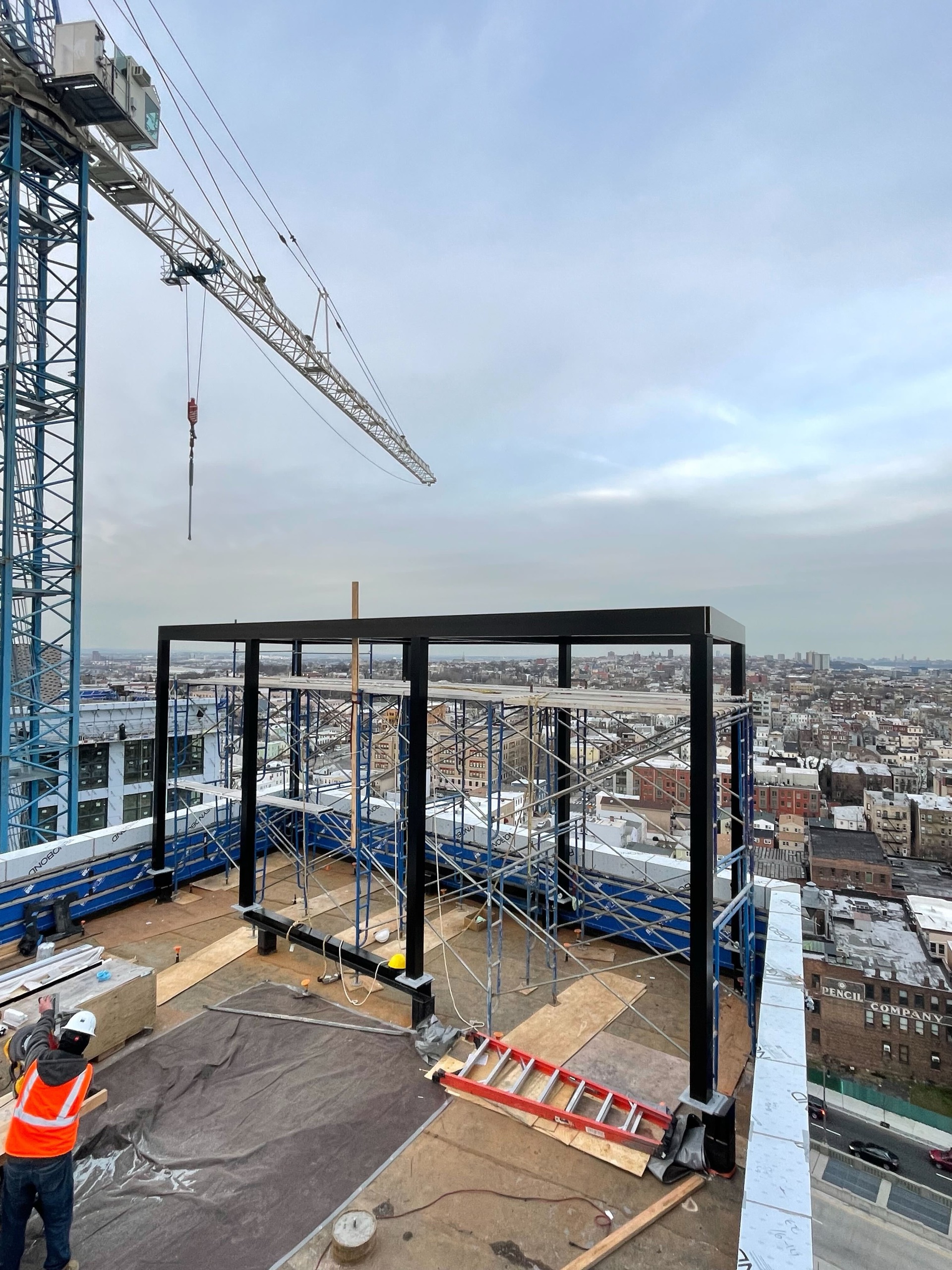 Black steel pergola frame under construction on a rooftop with a crane and city skyline