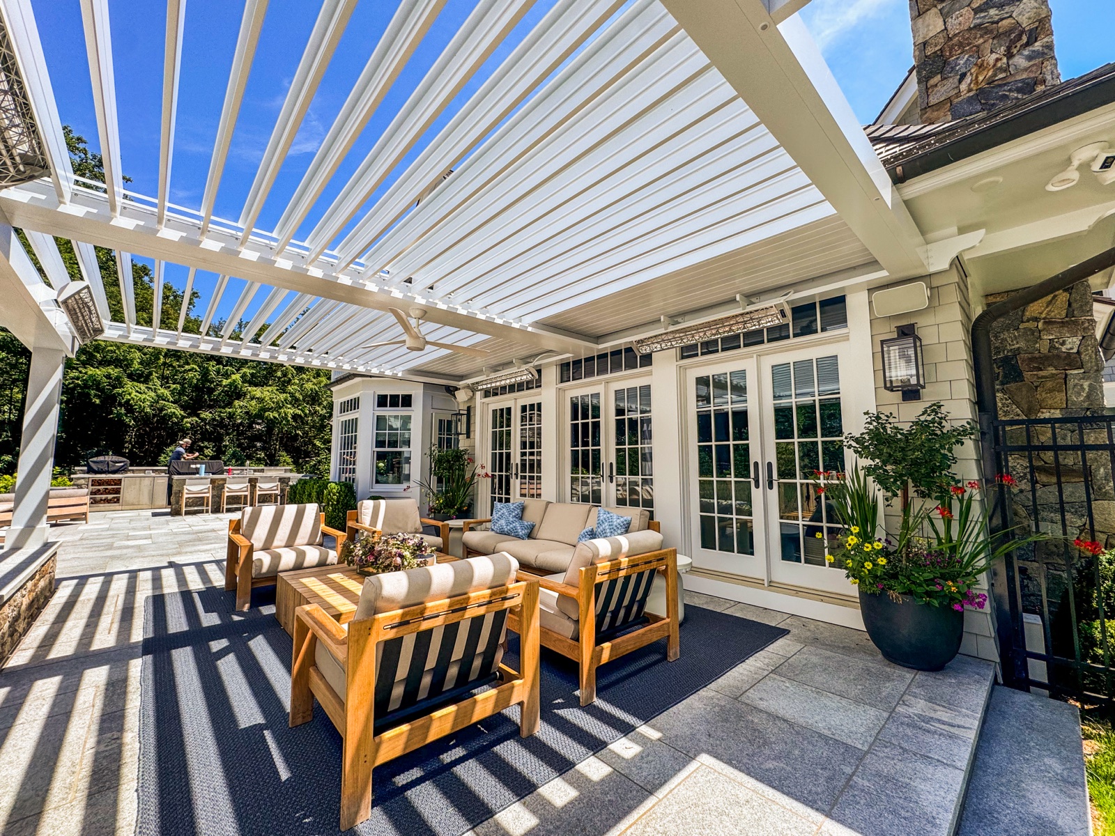 Louvered pergola beside French doors with teak lounge seating
