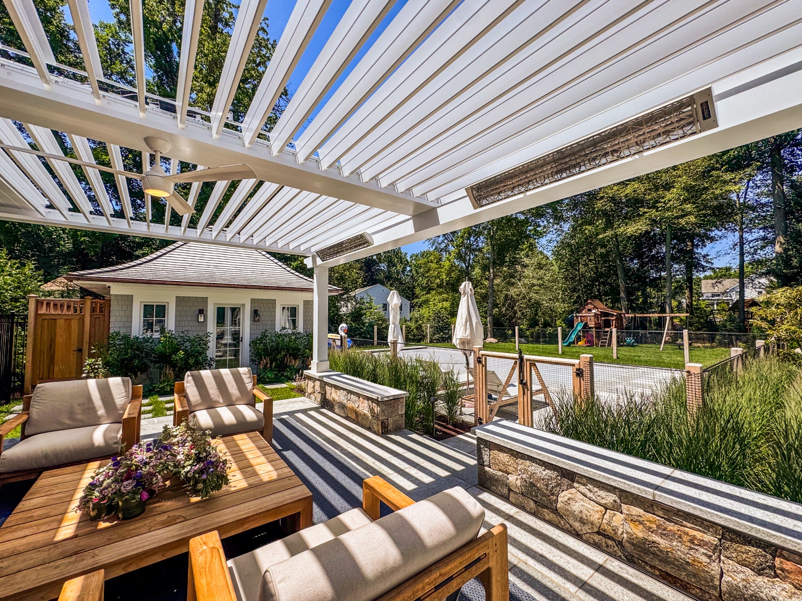 Open-louver pergola over the patio with outdoor kitchen and fireplace in Riverside, CT