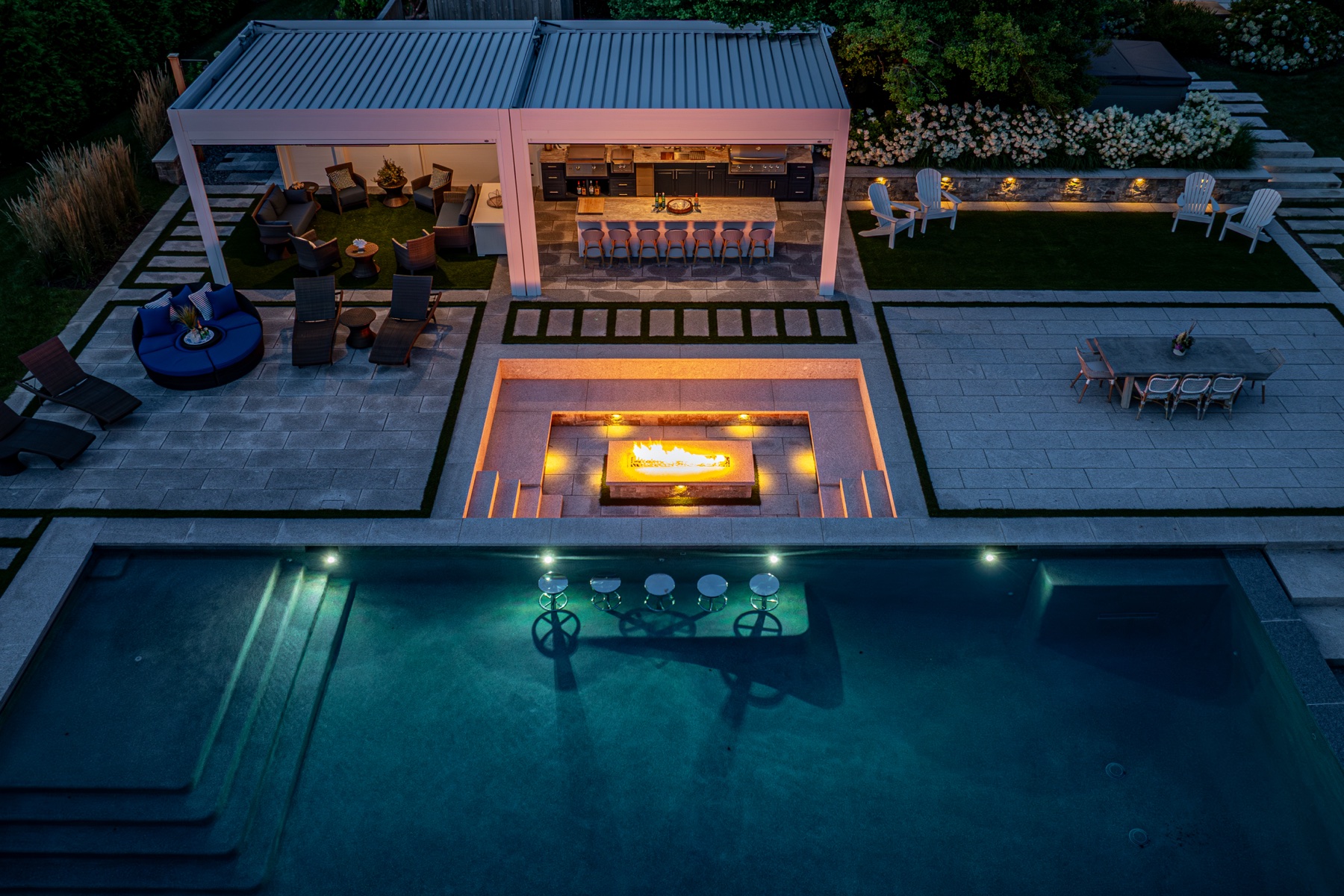 Night aerial of the louvered pergola, outdoor kitchen, fire feature and illuminated pool