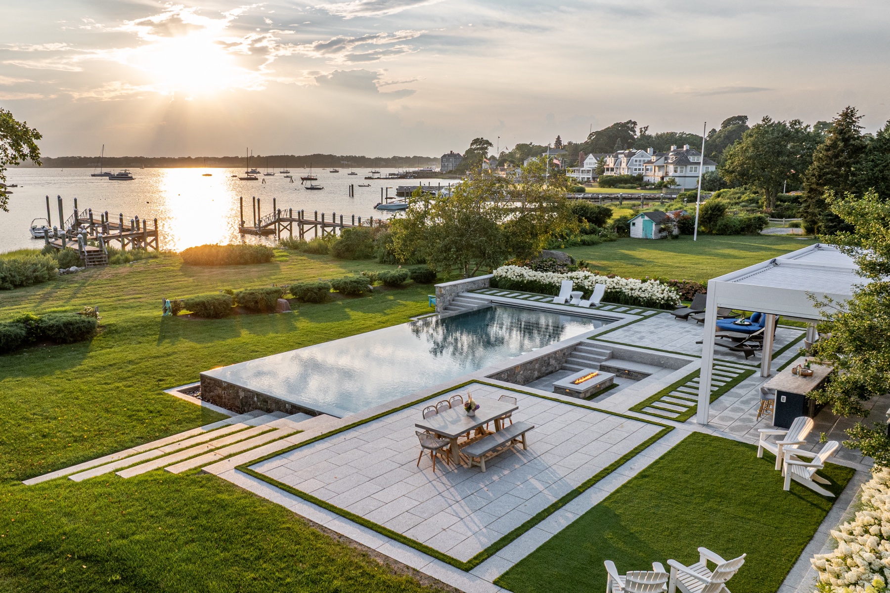 Sunset aerial over the bay — pool, pergola and dining terrace on the waterfront