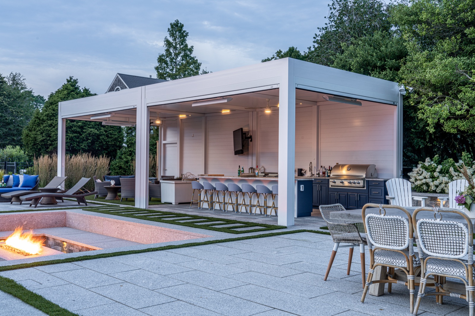 Motorized louvered pergola over the outdoor kitchen and bar, lit at dusk